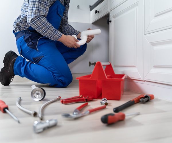 Male Plumber In Overall Fixing Kitchen Sink Pipe