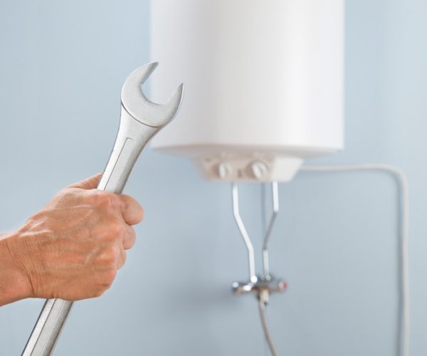 Close-up Of A Person's Hand Holding Spanner In Front Of Electric Boiler