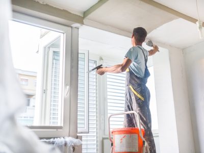 Thirty years old manual worker with wall plastering tools inside a house. Plasterer renovating indoor walls and ceilings with float and plaster.